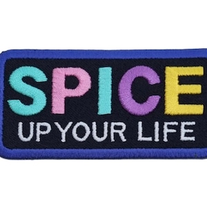 Peut inclure: Écusson brodé avec les mots "SPICE UP YOUR LIFE" en lettres colorées. Le patch a un fond bleu marine avec une bordure bleue et est de forme rectangulaire.