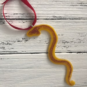 May include: A yellow glass Christmas ornament shaped like a snake with a red ribbon attached.