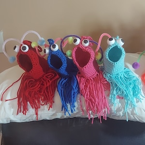 May include: Four crocheted finger puppets in the shape of a creature with long, stringy hair. The puppets are red, blue, pink, and turquoise.