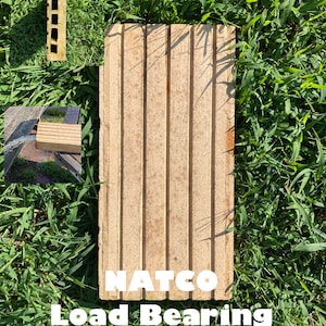 May include: A vintage NATCO load bearing structure block. The block is made of concrete and has a rough, textured surface. The block is brown and has a rectangular shape. The block is sitting on a bed of green grass.