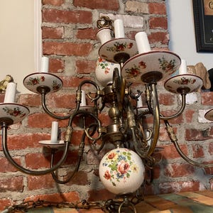 May include: A vintage chandelier with multiple arms and candle holders. The chandelier features a brass finish and ceramic accents with floral patterns in red, pink, and blue. The fixture hangs from a chain and has a decorative globe at the center.