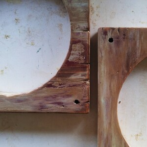 May include: Two rustic wooden frames with circular openings. The frames are made of weathered wood with a natural wood finish. The frames are slightly different sizes and are positioned next to each other.