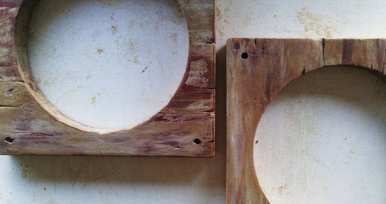 May include: Two rustic wooden frames with circular openings. The frames are made of weathered wood with a natural wood finish. The frames are slightly different sizes and are positioned next to each other.