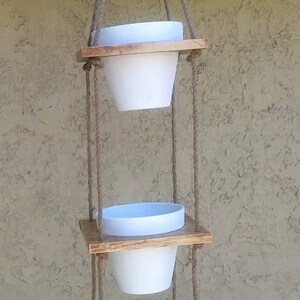May include: A three-tiered hanging planter made of wood with white ceramic pots. The planter is suspended from the ceiling with natural twine.
