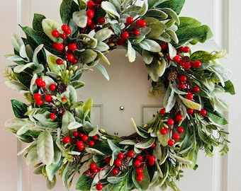 May include: A green and white Christmas wreath with red berries. The wreath is decorated with pine cones and greenery.