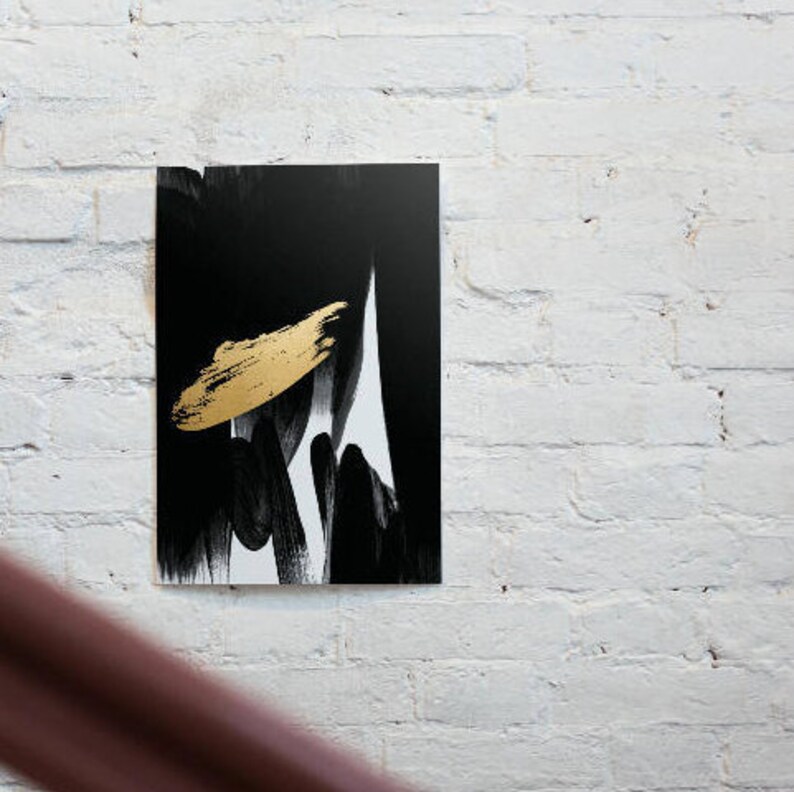 K&ouml;nnte beinhalten: Abstrakter Kunstdruck mit einem kr&auml;ftigen goldenen Pinselstrich vor einem schwarz-wei&szlig;en Hintergrund. Das Kunstwerk ist auf einer rechteckigen Leinwand montiert und an einer wei&szlig;en Backsteinmauer aufgeh&auml;ngt. Modernes, minimalistisches Design.