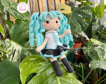 May include: Crocheted doll with long blue hair, wearing a white shirt, black skirt, and black boots. The doll is sitting on a green leaf.