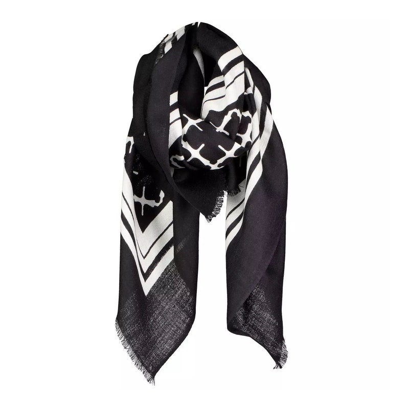 May include: A black and white patterned scarf. The scarf features a geometric design with white stripes and shapes against a black background. The scarf has a fringed edge and is draped, showcasing its design and texture.