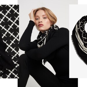 May include: Black and white patterned scarf. The scarf features a geometric design with a border of white lines. The scarf is draped around a person's neck and shoulders. The scarf is made of a soft, flowing fabric.