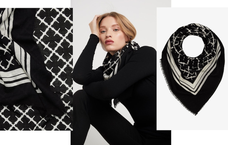 May include: Black and white patterned scarf. The scarf features a geometric design with a border of white lines. The scarf is draped around a person's neck and shoulders. The scarf is made of a soft, flowing fabric.