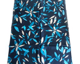 May include: A navy blue scarf with a repeating pattern of stylized leaves in shades of blue and white. The leaves are arranged in a floral-like design, creating a visually appealing and elegant accessory.