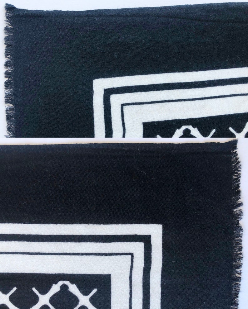 May include: Black and white patterned textile with a fringed edge. The design features a geometric border with a repeating pattern in the corner. The textile is likely a scarf or a decorative piece.