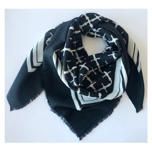 May include: A black and white square scarf with a geometric pattern. The scarf has a black background with a white geometric design in the center and white borders with a chevron pattern. The edges are fringed.
