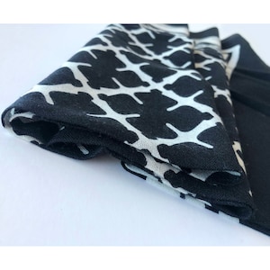 May include: Folded black and white patterned fabric, likely a scarf or handkerchief. The pattern is a repeating design of white shapes against a black background. The fabric is neatly folded, showcasing the contrasting colors and design.
