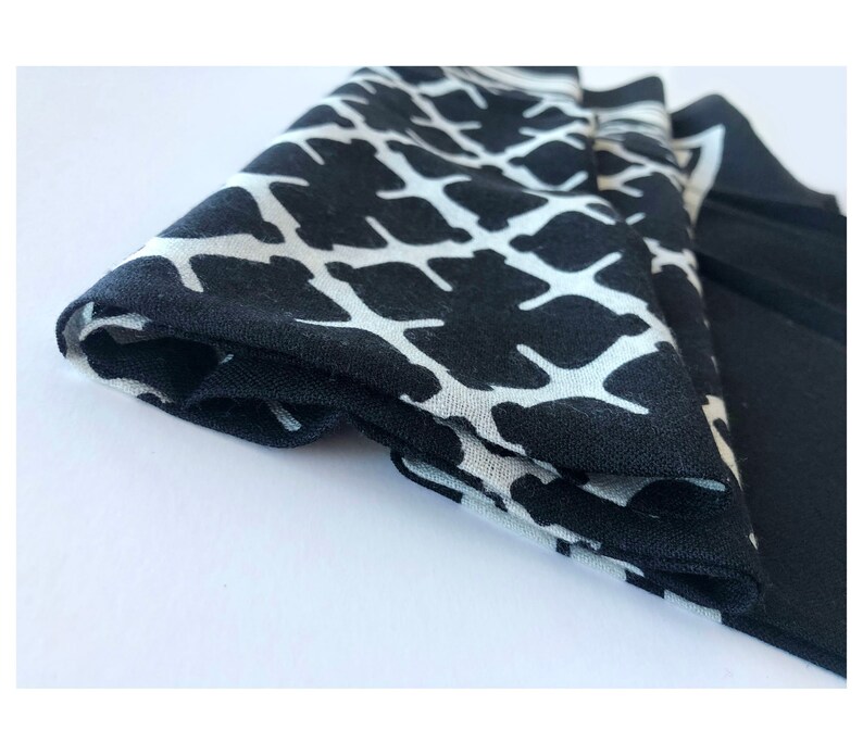 May include: Folded black and white patterned fabric, likely a scarf or handkerchief. The pattern is a repeating design of white shapes against a black background. The fabric is neatly folded, showcasing the contrasting colors and design.