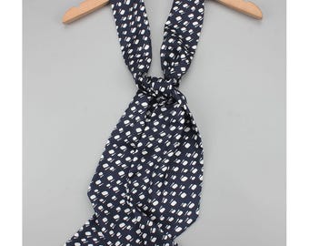 May include: A navy blue scarf with a white dotted pattern, knotted and displayed on a wooden hanger. The scarf's design features small, evenly spaced white dots against a dark blue background, creating a classic and versatile accessory.