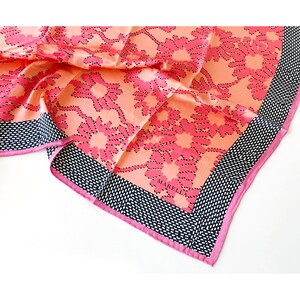 May include: A silk scarf featuring a floral design in pink and peach hues. It has a black and white dotted border and a pink trim. The brand name "MARELLA" is displayed on the scarf.