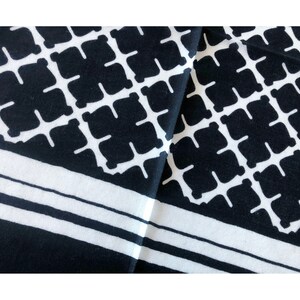 May include: Black and white patterned fabric with a geometric design. The pattern features a repeating grid of black squares with white cross-like shapes inside. The fabric also has white stripes along the edges.