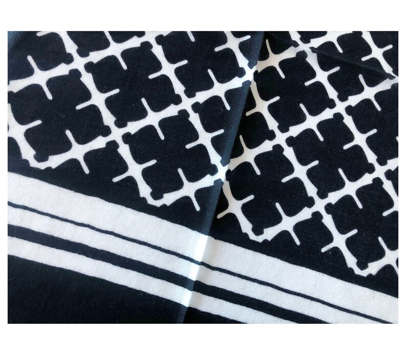 May include: Black and white patterned fabric with a geometric design. The pattern features a repeating grid of black squares with white cross-like shapes inside. The fabric also has white stripes along the edges.