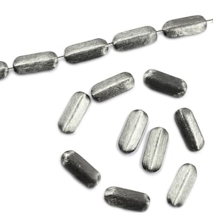 May include: A strand of silver-toned metal beads, with a few beads scattered around it. The beads are oval-shaped and have a brushed finish.