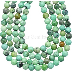 May include: A strand of green turquoise beads, each bead is round and has a mottled pattern. The beads are strung together to form a long necklace.