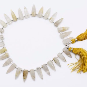 May include: A strand of white and yellow gemstone beads with a pointed, teardrop shape. The beads are strung on a silver wire and have a tassel on each end.