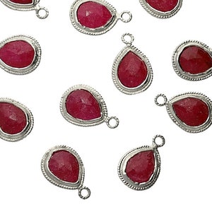 May include: Ten red gemstone teardrop charms with silver settings. Each charm has a small loop for attaching to jewelry.