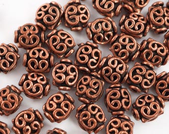 May include: A collection of copper-colored metal beads with a decorative swirl design. The beads are oval-shaped and have a smooth, shiny finish.