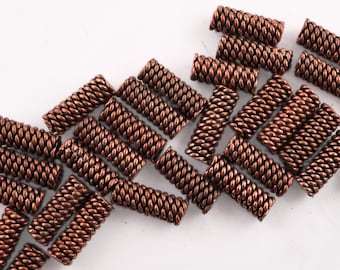 May include: A group of copper-colored metal beads with a braided or twisted design. The beads are scattered on a white surface.
