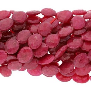 May include: A strand of oval-shaped, faceted, red gemstone beads. The beads are smooth and polished, with a slight sparkle.