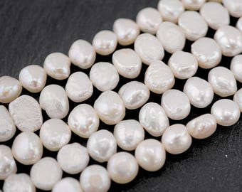 May include: A strand of white, oval-shaped freshwater pearls. The pearls are arranged in rows, creating a layered effect. The pearls are smooth and lustrous.
