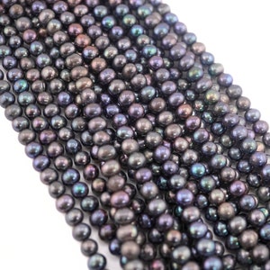 May include: A strand of black freshwater pearls with iridescent hues. The pearls are round and smooth, and they are strung on a clear thread.