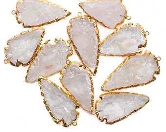 May include: Ten white quartz arrowhead pendants with gold-plated edges. The arrowheads are arranged in a cluster on a white background.