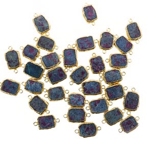 May include: Rectangular gemstone connectors with a gold-coloured bezel. The gemstones have a mix of dark blue and red hues. Each connector has two small loops for attaching to other jewellery components. The connectors are scattered on a white background.
