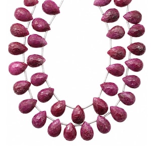 May include: Two strands of faceted, teardrop-shaped ruby gemstones strung on a silver wire. The rubies are a deep, rich red color with a textured surface. The gemstones are displayed against a white background.