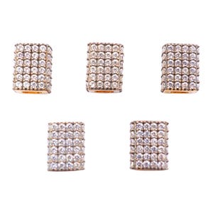 May include: Five gold-toned, rectangular jewelry beads encrusted with numerous clear, sparkling crystals. The beads are arranged against a white background, showcasing their intricate design and reflective surfaces. The crystals are tightly packed, creating a dazzling effect.