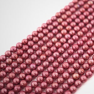 May include: A strand of pink freshwater pearls. The pearls are round and have a smooth, iridescent finish.