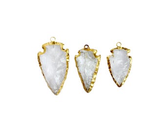 May include: Three gold-rimmed arrowhead pendants made of clear quartz. The arrowheads are different sizes, with the largest being at the top of the image.
