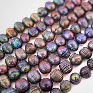 May include: A strand of iridescent black freshwater pearls. The pearls are oval shaped and have a smooth, glossy finish.
