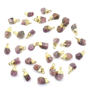 May include: A collection of 30 pink and gold gemstone pendants. Each pendant features a raw, natural gemstone with a gold-plated bail. The gemstones are various shades of pink and have a rough, irregular shape.