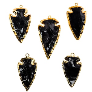 May include: Five black arrowhead pendants with gold trim. The arrowheads are all the same shape and size, and they have a textured surface.