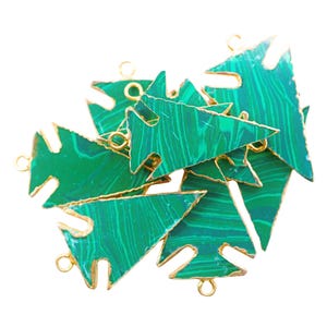 May include: A collection of green malachite gemstone pendants in a Christmas tree shape. Each pendant has a gold-colored trim and small loops for attaching to jewelry. The malachite has a natural, swirled pattern.