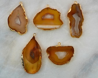 May include: Five agate pendant charms with gold-plated edges. The agate is a light brown color with white and brown banding. The pendants are various shapes, including teardrop, oval, and irregular.