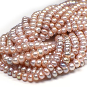 May include: Close-up of a collection of pink freshwater pearls. The pearls are small, round, and have a lustrous sheen. The strands are tightly packed together, creating a dense, textured appearance. The overall color is a soft, muted pink with hints of iridescent hues.