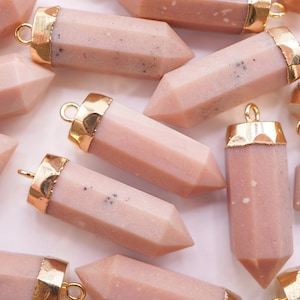 May include: A group of pink crystal point pendants with gold-toned metal caps. The pendants are scattered on a white surface.
