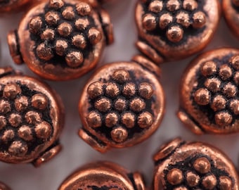 May include: A close-up of a group of copper-colored beads with a textured, raised pattern. The beads are round and have a slightly irregular shape.