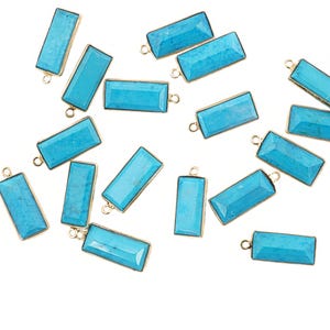 May include: Rectangular turquoise gemstone pendants with gold-colored metal frames. Each pendant has a small loop at the top for attaching to jewelry. The pendants are scattered on a white background.