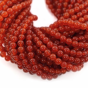 May include: A strand of round, orange carnelian beads. The beads are smooth and polished, and they have a natural, earthy look.