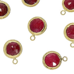 May include: Six gold-toned pendant charms with red gemstone cabochons. Each charm has a round, rope-like border and a small loop at the top.