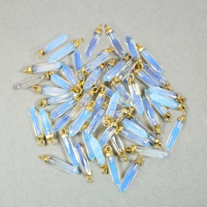 May include: A pile of light blue crystal point pendants with gold-toned jump rings. The pendants are approximately 1 inch long.